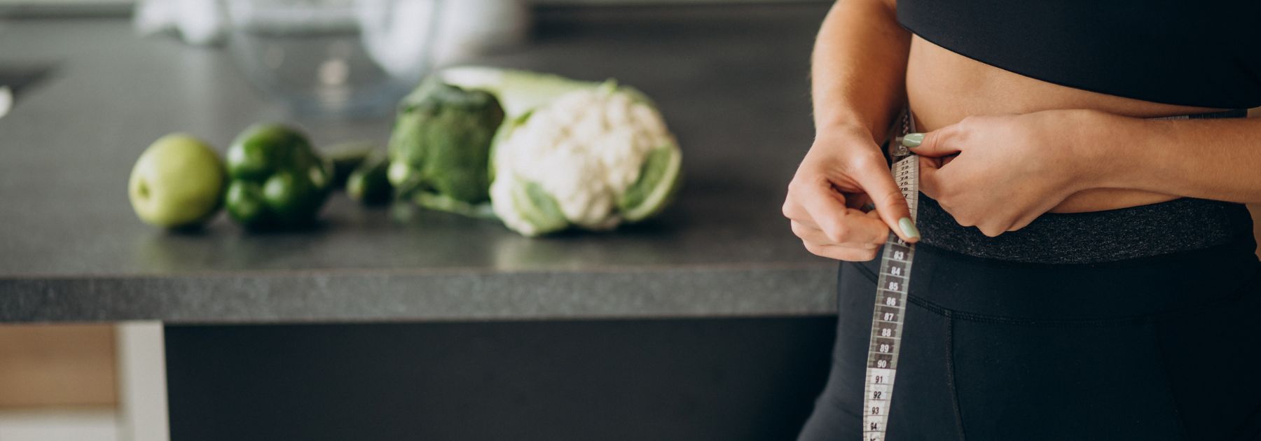 woman holding tape measure around her waist with healthy green vegetables in the background